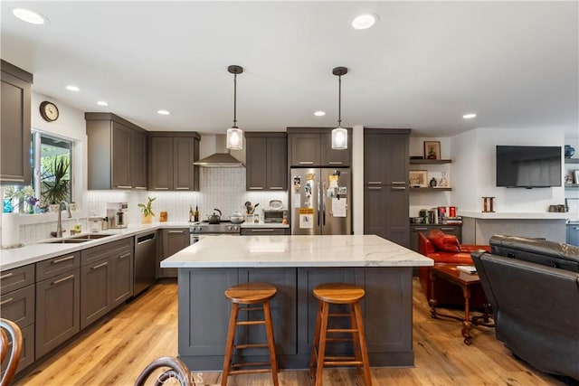 kitchen featuring stainless steel appliances, a sink, open floor plan, wall chimney range hood, and a center island