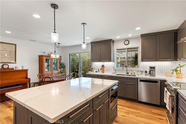 kitchen with a sink, light wood-style floors, appliances with stainless steel finishes, tasteful backsplash, and decorative light fixtures