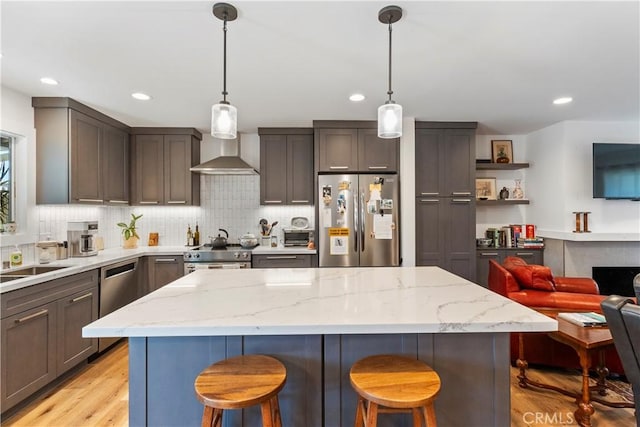 kitchen featuring stainless steel appliances, a kitchen breakfast bar, light stone countertops, wall chimney exhaust hood, and tasteful backsplash