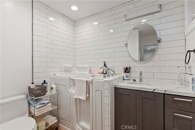 bathroom with toilet, tasteful backsplash, tile walls, and vanity