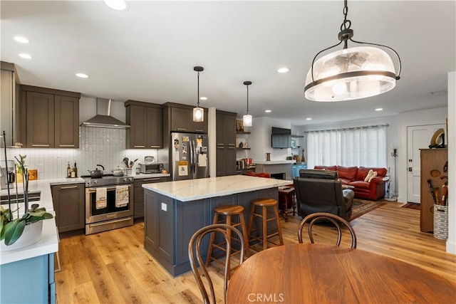 kitchen featuring stainless steel appliances, a breakfast bar, light wood-style floors, backsplash, and wall chimney exhaust hood