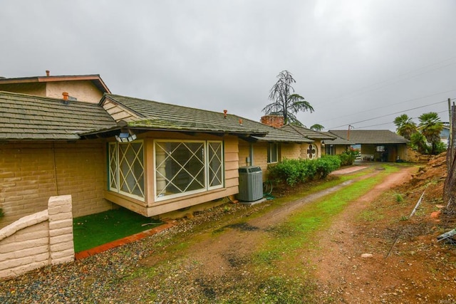 back of property featuring dirt driveway, central AC, and brick siding