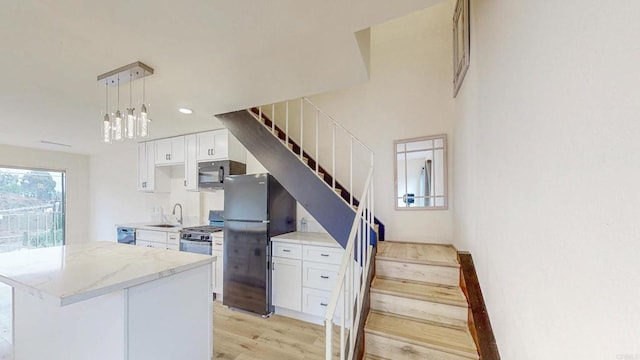 kitchen with white cabinets, light wood finished floors, black appliances, and light stone countertops