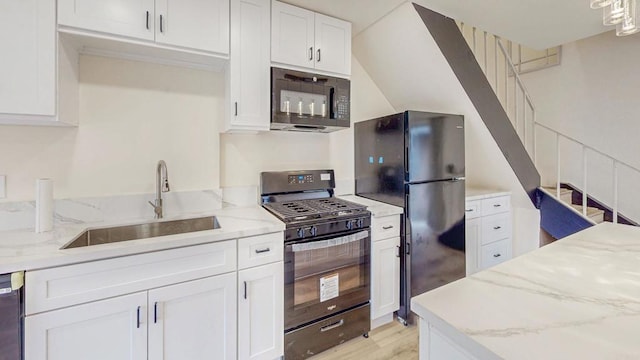 kitchen with light stone countertops, black appliances, white cabinets, and a sink