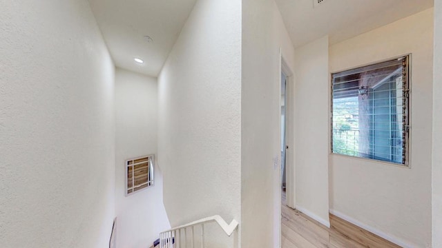 hall featuring a textured wall, light wood-style flooring, and baseboards