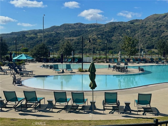 view of swimming pool with a forest view, a patio area, fence, and a mountain view