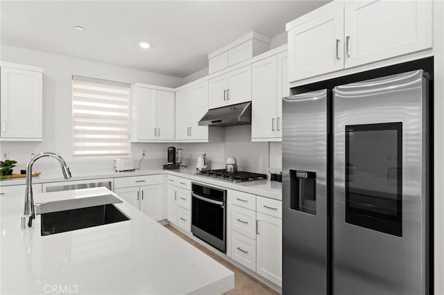 kitchen featuring under cabinet range hood, stainless steel appliances, a sink, white cabinets, and light countertops