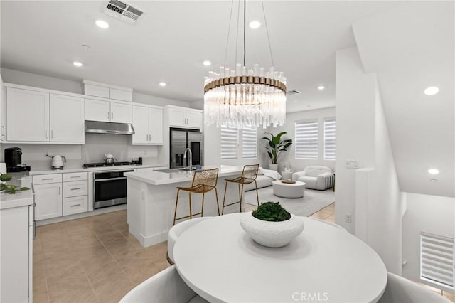 kitchen featuring under cabinet range hood, visible vents, light countertops, appliances with stainless steel finishes, and an island with sink