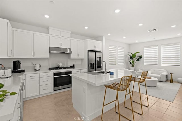 kitchen featuring light tile patterned flooring, under cabinet range hood, a sink, visible vents, and appliances with stainless steel finishes