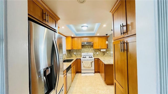 kitchen featuring under cabinet range hood, stainless steel appliances, ornamental molding, brown cabinets, and a raised ceiling