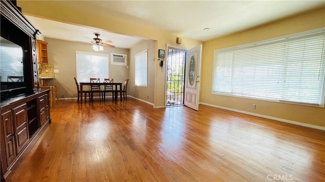 interior space with a wall mounted air conditioner, ceiling fan, baseboards, and wood finished floors