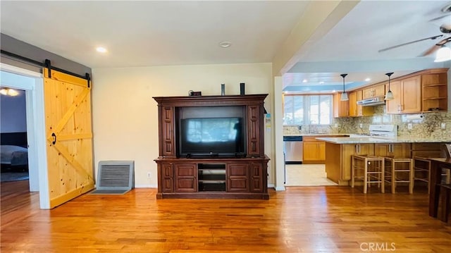 unfurnished living room featuring a barn door, visible vents, ceiling fan, light wood-type flooring, and recessed lighting