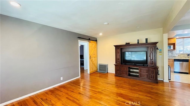 unfurnished living room featuring visible vents, a barn door, light wood-style flooring, and baseboards