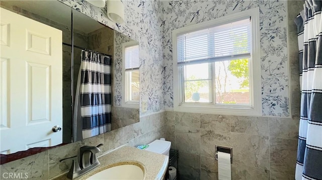 full bathroom with wallpapered walls, vanity, tile walls, and a wainscoted wall