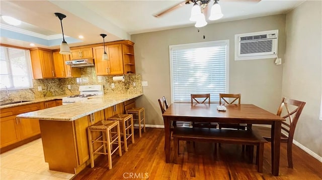 kitchen featuring tasteful backsplash, white range with gas stovetop, a breakfast bar area, under cabinet range hood, and a sink