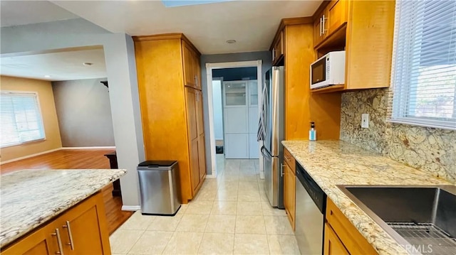 kitchen with light stone counters, appliances with stainless steel finishes, brown cabinets, and decorative backsplash