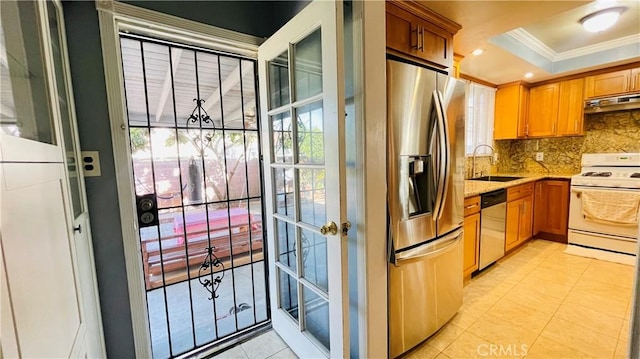 kitchen featuring appliances with stainless steel finishes, ornamental molding, a tray ceiling, under cabinet range hood, and a sink