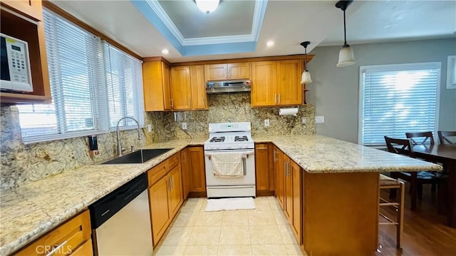 kitchen with a raised ceiling, a sink, white appliances, a peninsula, and under cabinet range hood