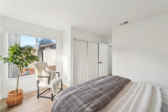 bedroom with light wood-type flooring, baseboards, visible vents, and a closet