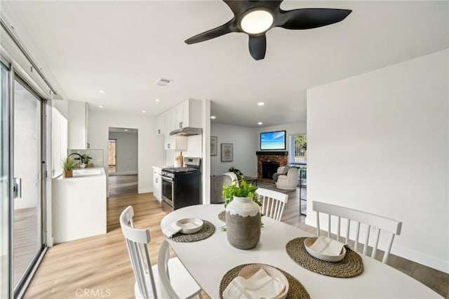 dining room with light wood-style floors, a fireplace, visible vents, and recessed lighting