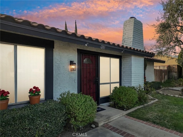 property entrance with a chimney, fence, a tile roof, and stucco siding