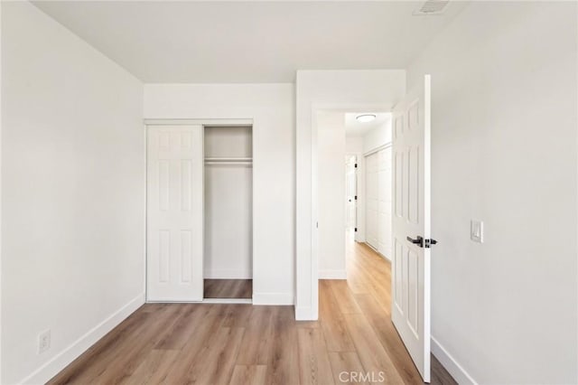 unfurnished bedroom with light wood finished floors, visible vents, baseboards, and a closet