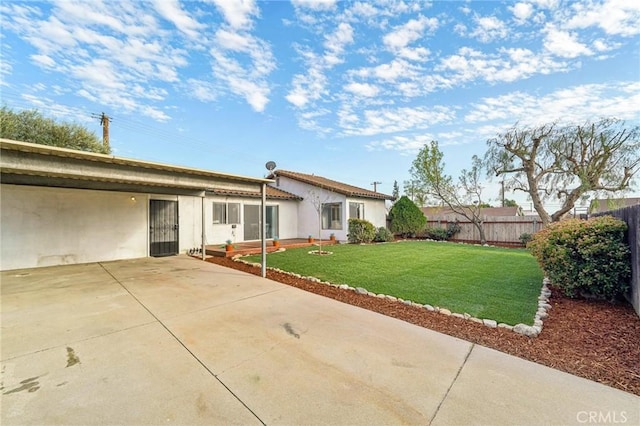 rear view of property with a yard, fence, and stucco siding