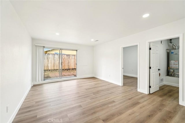 empty room featuring water heater, light wood-type flooring, and baseboards