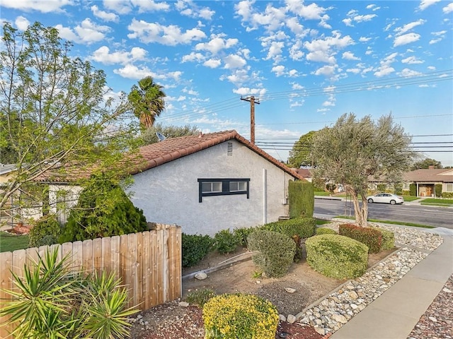 view of property exterior featuring a tiled roof, fence, and stucco siding