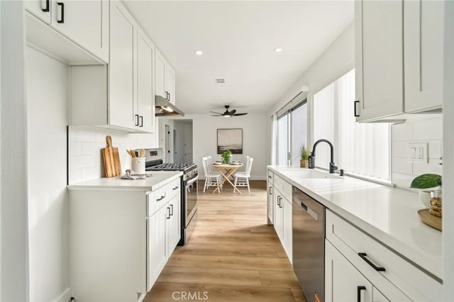 kitchen featuring light wood-style floors, stainless steel appliances, light countertops, under cabinet range hood, and a sink