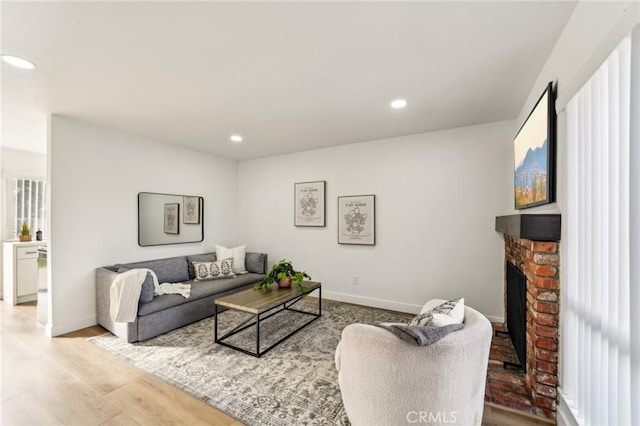 living area featuring recessed lighting, a brick fireplace, light wood-style flooring, and baseboards