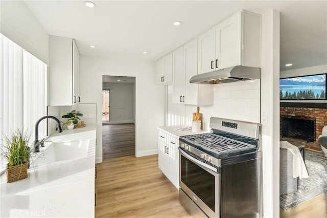 kitchen with light wood-style flooring, backsplash, stainless steel gas stove, a sink, and under cabinet range hood