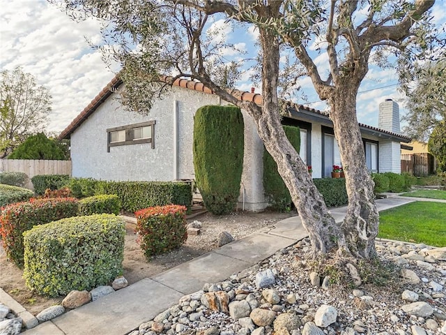 view of side of home with a tiled roof, a chimney, fence, and stucco siding