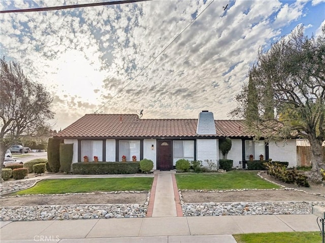 view of front of home featuring a chimney, a tiled roof, a front lawn, and stucco siding