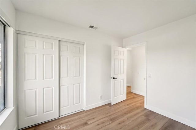 unfurnished bedroom with a closet, wood finished floors, visible vents, and baseboards