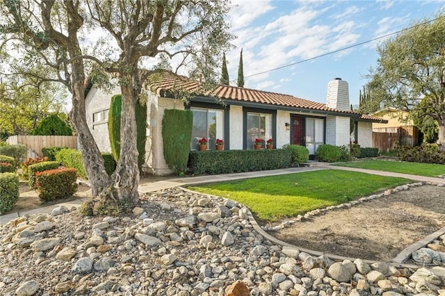 view of front of house featuring a chimney, stucco siding, a front yard, fence, and a tiled roof