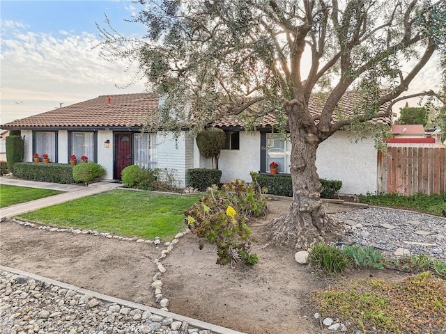 view of front of house featuring a front yard, a tile roof, fence, and stucco siding