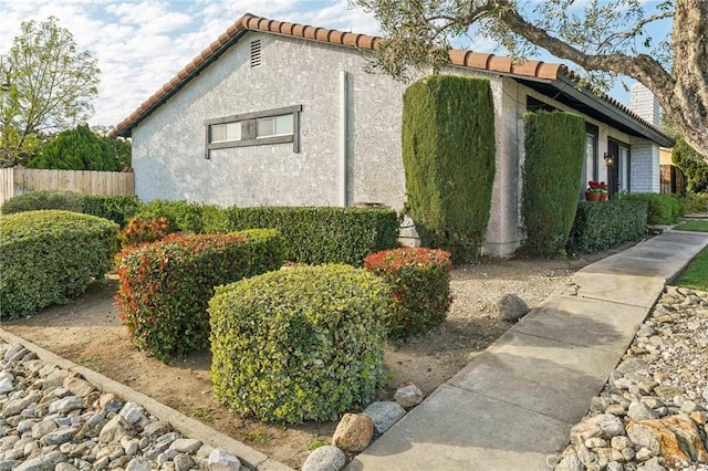 view of property exterior featuring a tiled roof, fence, and stucco siding