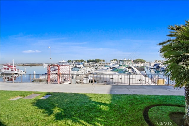 dock area with a water view, fence, and a yard