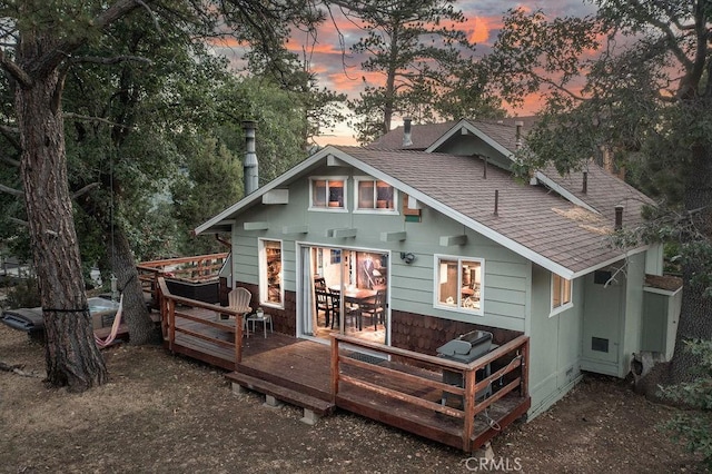 back of house at dusk with a shingled roof and a deck
