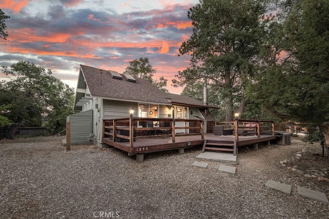 back of property at dusk with roof with shingles and a wooden deck