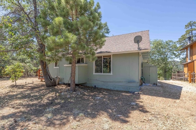 back of property with a shingled roof, crawl space, and fence