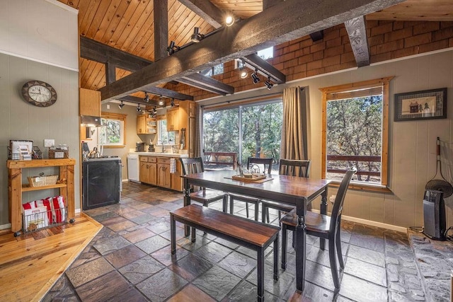 dining area featuring beam ceiling, stone tile flooring, rail lighting, wooden ceiling, and baseboards