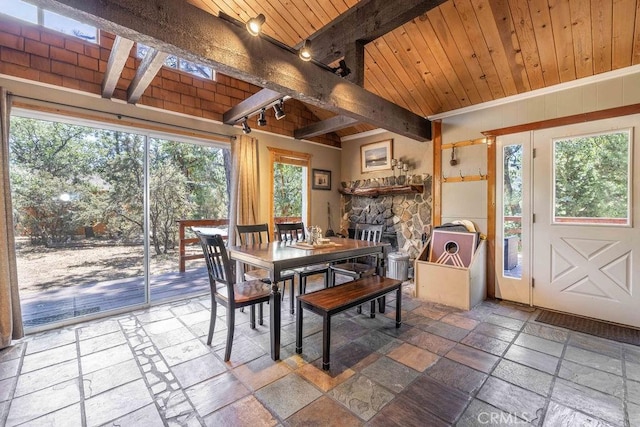 dining room with beam ceiling, a fireplace, stone tile floors, rail lighting, and wooden ceiling