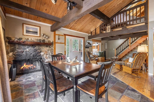 dining area featuring vaulted ceiling with beams, wood ceiling, a fireplace, and stairs