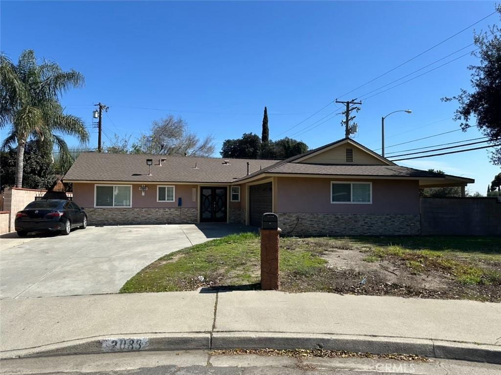 ranch-style home with an attached garage, fence, stone siding, driveway, and stucco siding