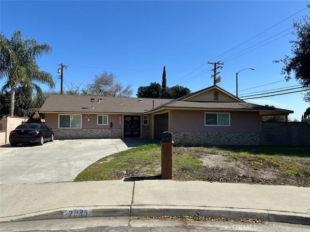 ranch-style home with an attached garage, fence, stone siding, driveway, and stucco siding