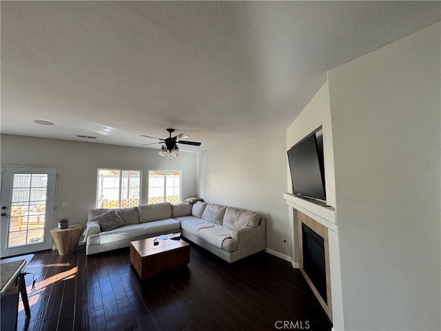 living area featuring visible vents, dark wood finished floors, ceiling fan, a textured ceiling, and a fireplace