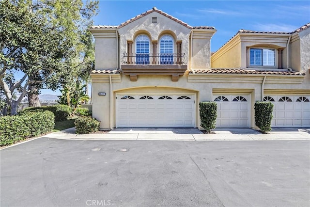 mediterranean / spanish-style house featuring a tiled roof, a balcony, an attached garage, and stucco siding