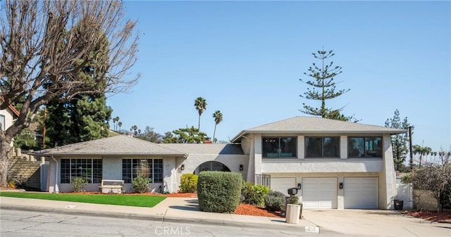 split level home featuring driveway, an attached garage, and stucco siding